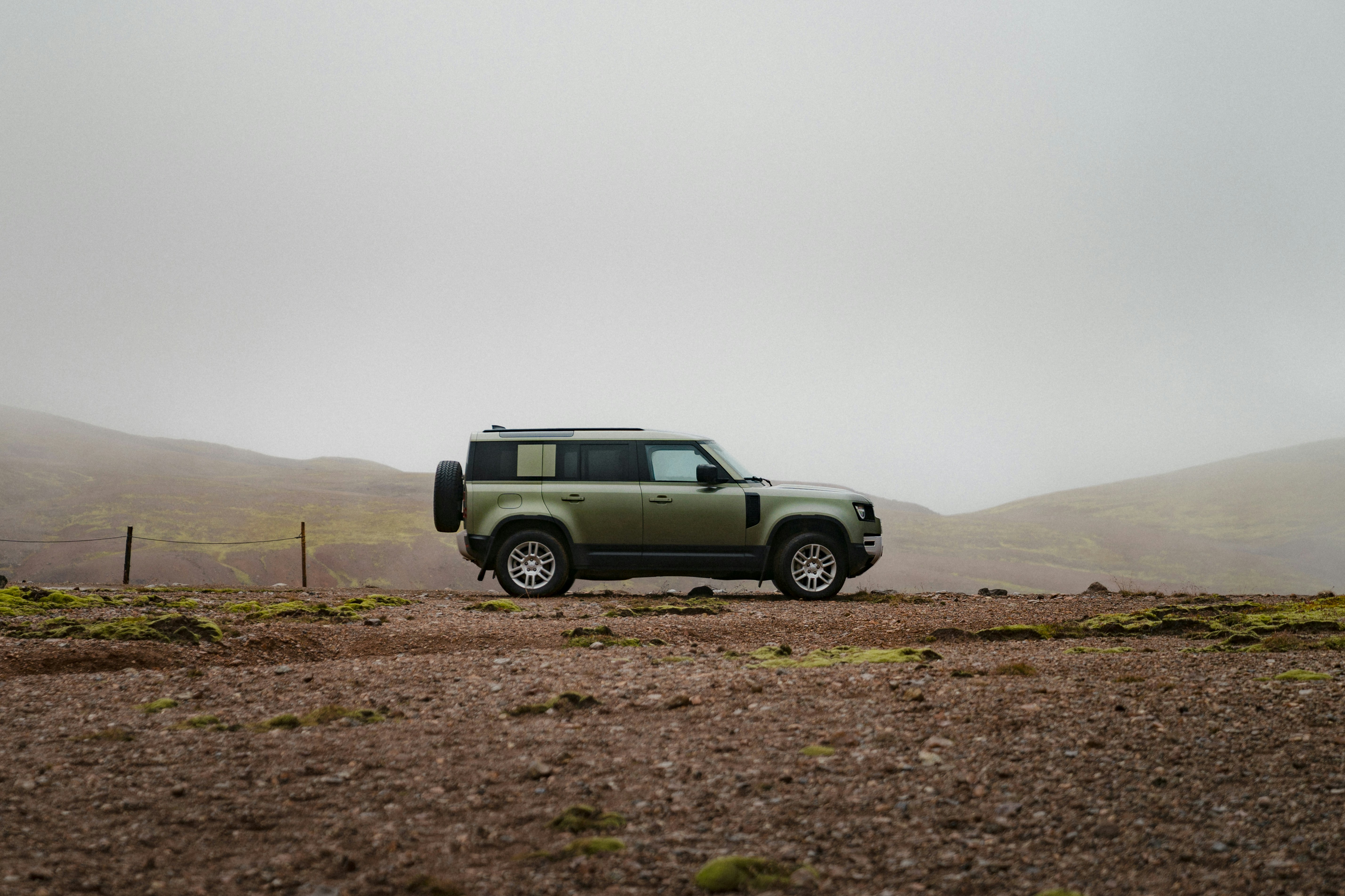 Een groen terreinvoertuig geparkeerd in een rotsachtig landschap onder een mistige hemel.